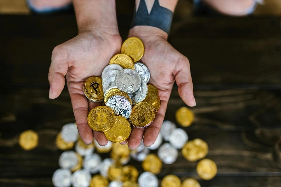 A person's hands holding a pile of various cryptocurrencies